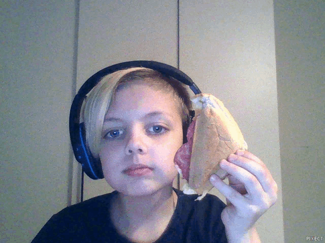 a young boy wearing headphones holds a sandwich in front of his head