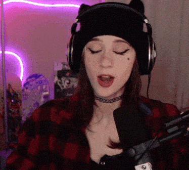 a woman wearing headphones and a choker sings into a microphone