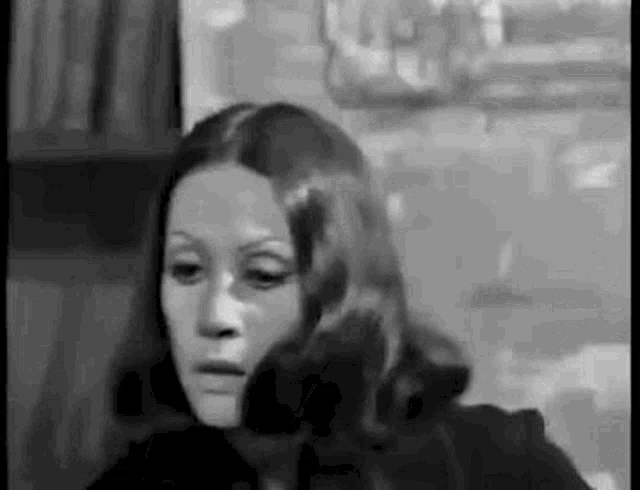 a black and white photo of a woman with long hair and a serious look on her face .