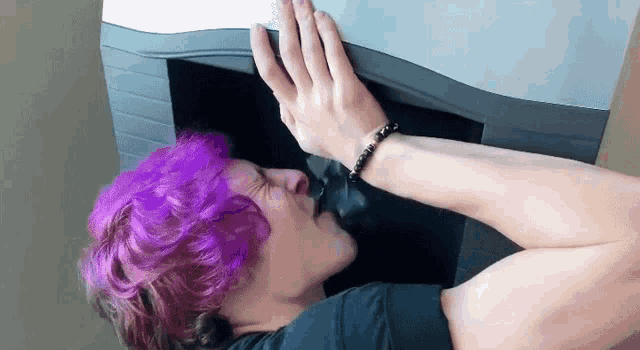 a man with purple hair is kissing a cat