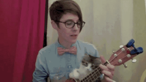 a man with glasses and a bow tie is playing an ukulele with a cat on it 's back .