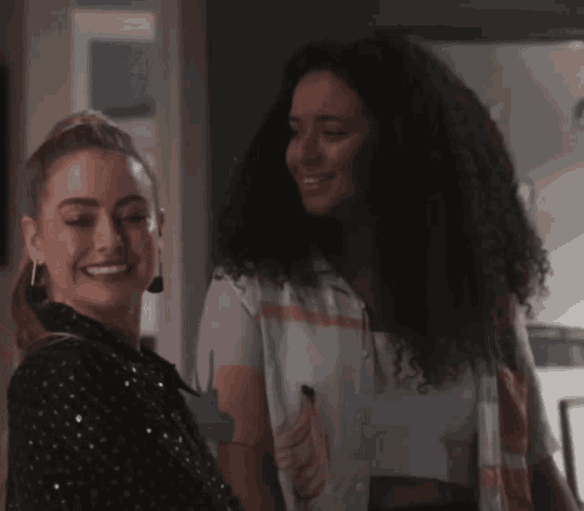 two women are looking at each other and smiling while standing next to each other