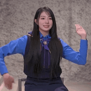 a girl in a blue shirt and vest is sitting in a chair with her arms outstretched and smiling .