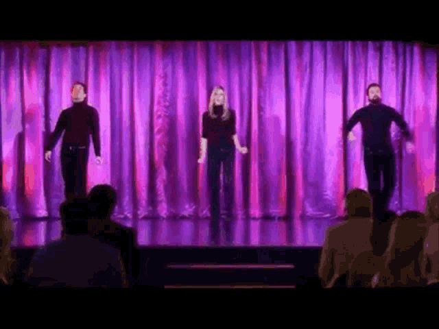 a group of people standing on a stage with purple curtains behind them