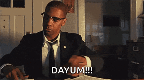 a man in a suit and tie is sitting at a desk and saying dayum