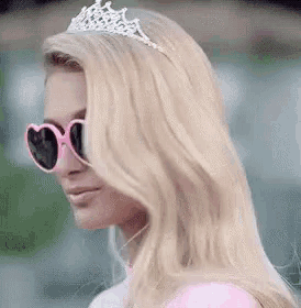 a woman wearing sunglasses and a tiara is standing in front of a green background .