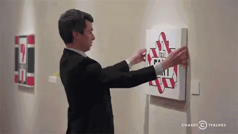 a man in a suit is hanging a painting on a wall that says comedy central