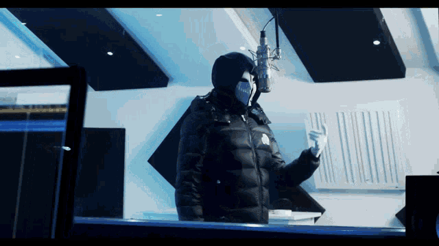 a man wearing a mask stands in front of a microphone in a recording studio