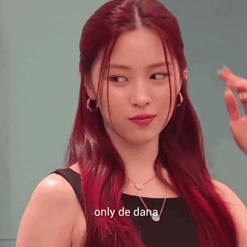 a woman with red hair is wearing a black dress and a necklace and says only de dana .