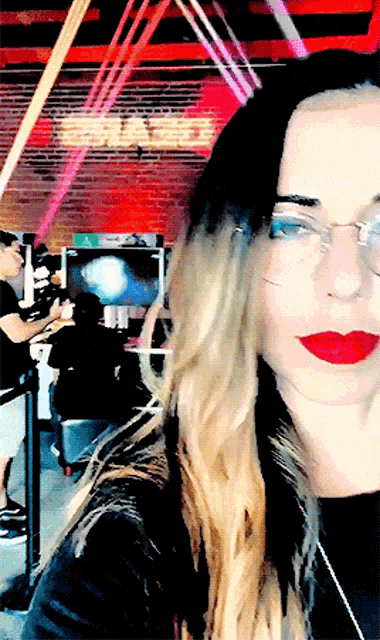 a woman wearing glasses and red lipstick takes a selfie in front of a sign that says smack