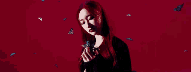 a woman with red hair is holding a butterfly in her hands