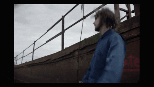 a man in a blue jacket is standing in front of a wall that says tate