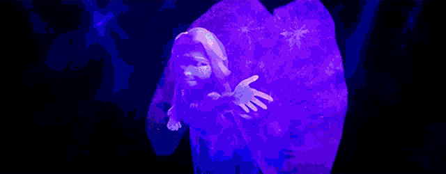 elsa from the movie frozen is standing in front of a purple object with her arms outstretched .