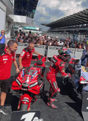 a man on a red lenovo motorcycle stands in front of a crowd
