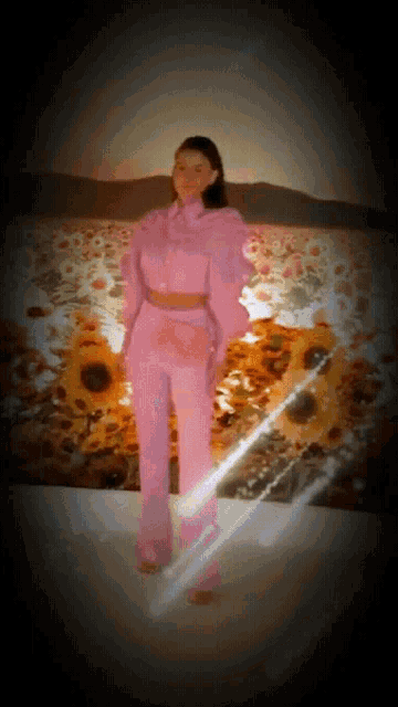 a woman in a pink jumpsuit stands in front of a field of sunflowers