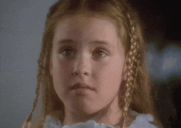 a little girl with braided hair and a white dress looks at the camera