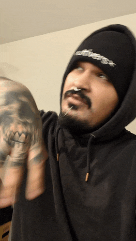 a man with a tattoo on his arm wears a black hoodie and a black beanie with the word ecstasy on it