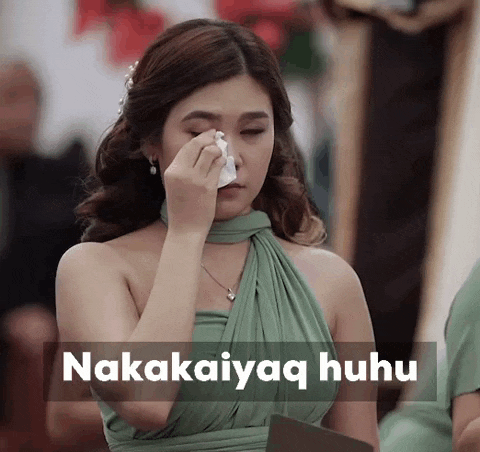 a woman in a green dress wipes her face with a napkin and the words nakaaiyaq huhu are visible behind her