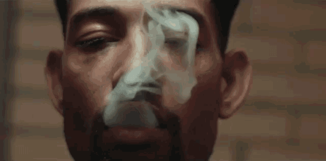 a man with a beard is smoking a cigarette with smoke coming out of his mouth .