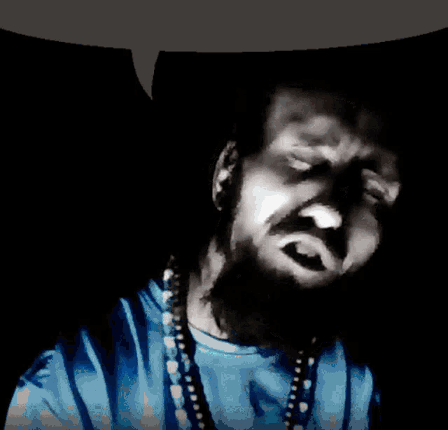 a man with a beard is wearing a blue shirt and necklace