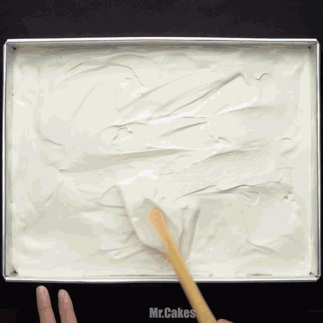 a person is spreading frosting on a pan that says mr.cakes on the bottom right