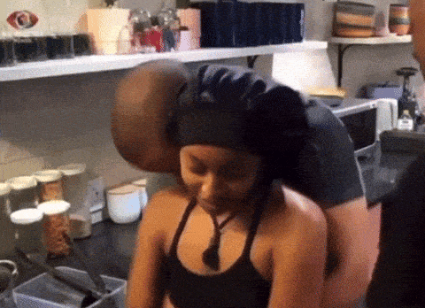 a man kissing a woman 's neck in a kitchen with a lot of jars on the shelves