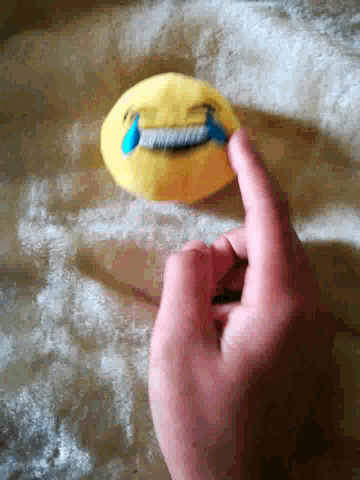 a person 's hand is pointing to a yellow smiley face