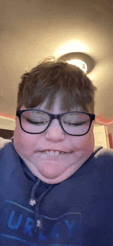 a boy wearing glasses and a hurley shirt makes a face