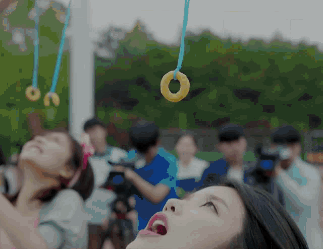 a woman looks up at a donut hanging from a blue string