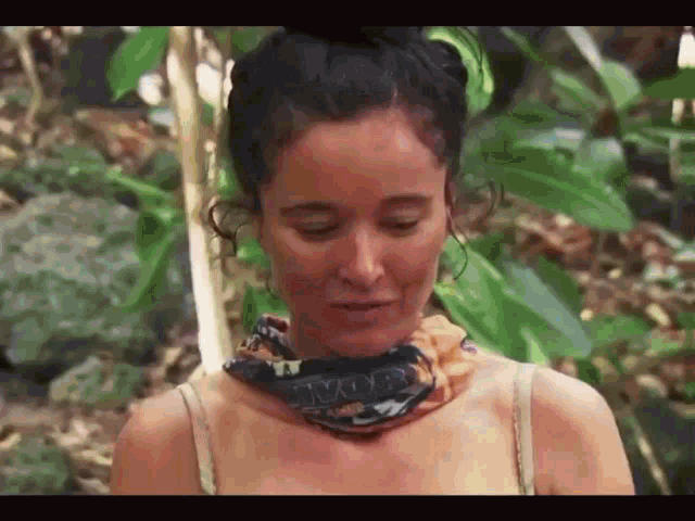 a woman wearing a scarf around her neck is standing in a forest .