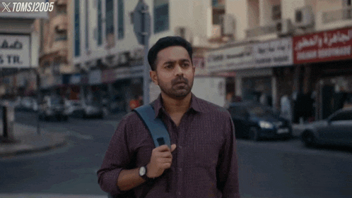 a man with a backpack is walking down a street with a sign that says toms 2005 in the background