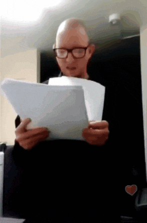 a bald man wearing glasses is reading a paper