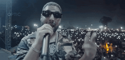 a man wearing sunglasses is singing into a microphone with optic written on the bottom