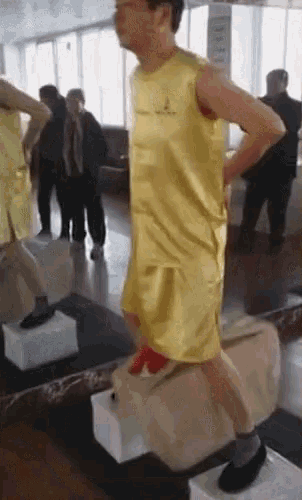 a man in a yellow tank top and shorts is standing in front of a mirror in a gym