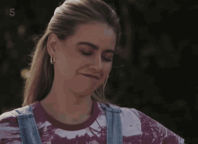 a woman wearing overalls and a tie dye shirt has the number 5 above her
