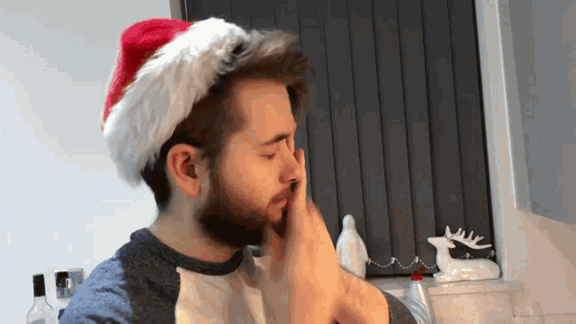 a man wearing a santa hat wipes his nose with his hands