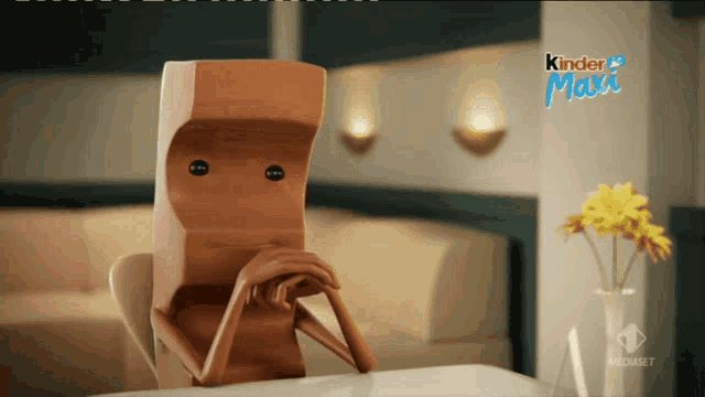 a cartoon character is sitting at a table with a kinder maxi sign behind him