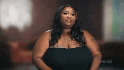 a woman with very large breasts is wearing a black dress and standing in a room .