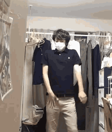 a man wearing a mask is standing in a room with clothes hanging on a rack