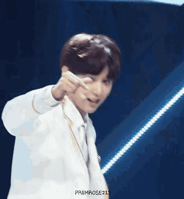 a young man in a white suit is pointing at the camera .