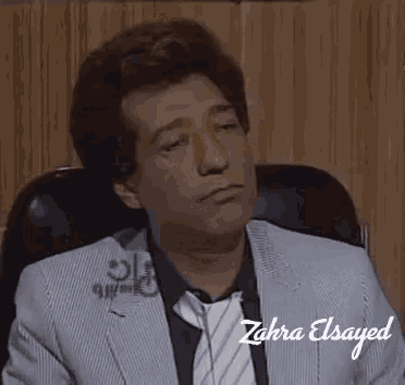 a man in a suit and tie sits in a chair with his eyes closed .