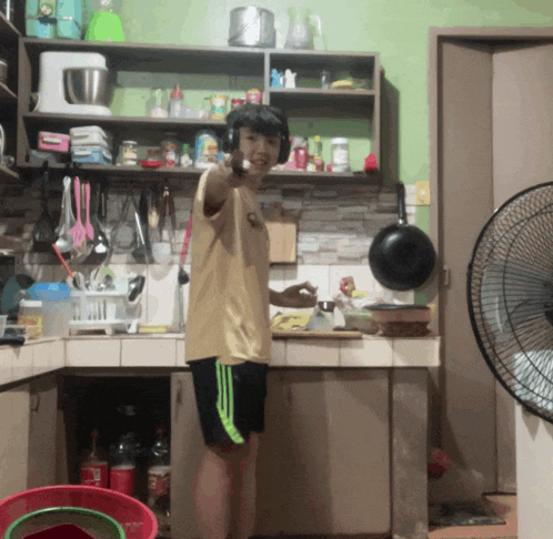 a man wearing headphones stands in a kitchen pointing at something