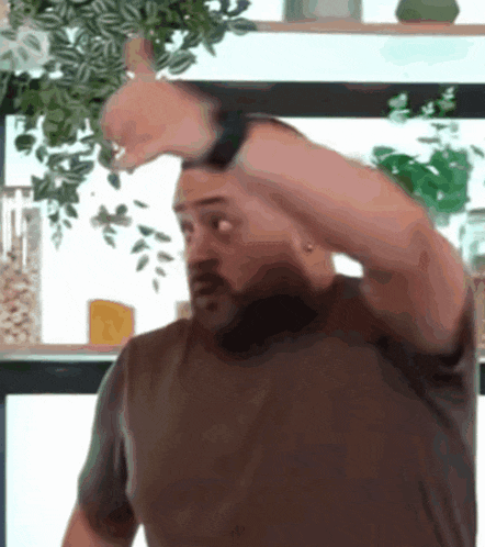 a man in a brown shirt is making a funny face with his hand on his head