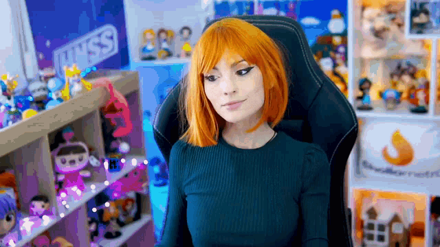 a woman with orange hair is sitting in a gaming chair in front of a shelf full of figurines .