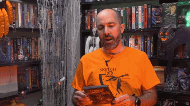 a man wearing an orange shirt that says sketch-22 is reading a book