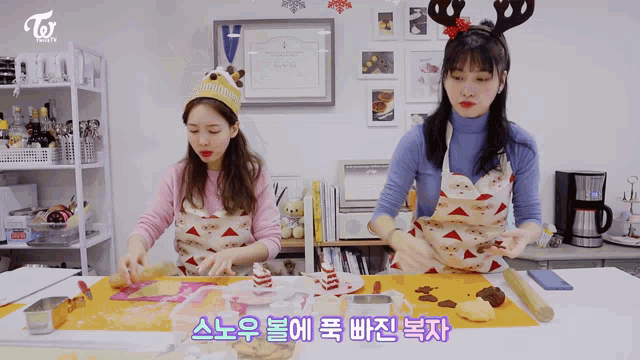 two women wearing aprons are preparing food in a kitchen and one has a reindeer headband on