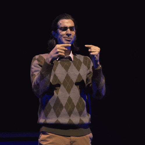 a man wearing glasses and a plaid sweater is making a funny face