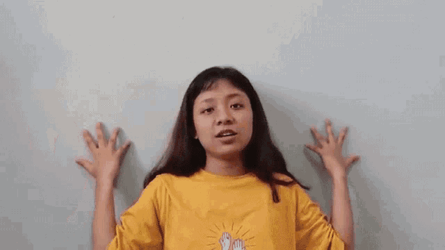 a young woman in a yellow shirt is making a funny face with her hands .
