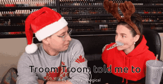 a man wearing a santa hat is talking to a woman with reindeer antlers on her head