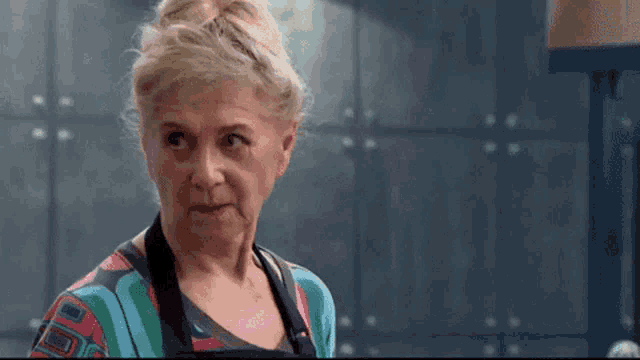 an elderly woman wearing an apron and a colorful shirt is making a funny face .